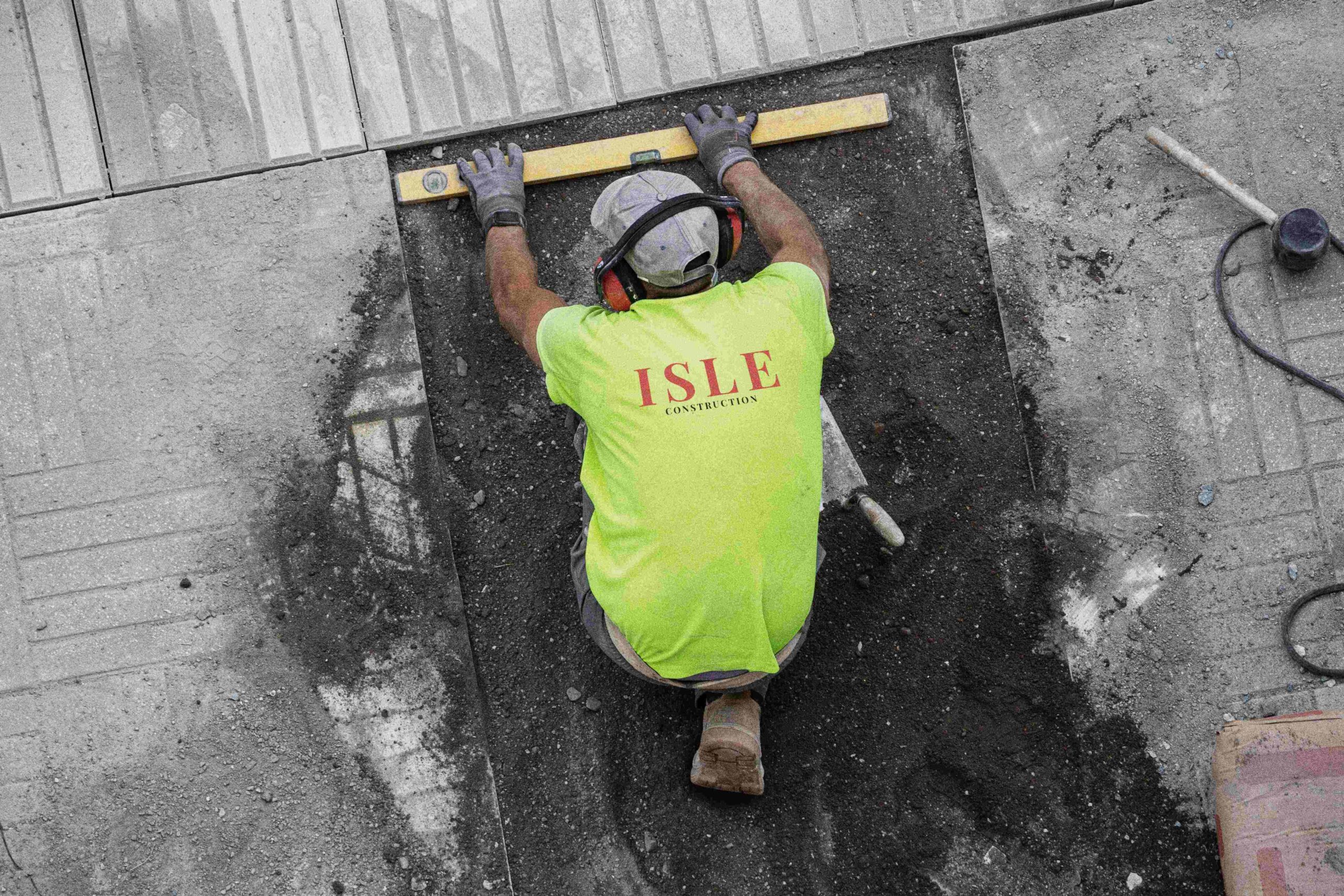 Image of constrcution work laying concrete on the ground, wearing a neon green work shirt with Isle Construction Logo